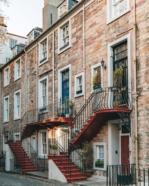 A multi-storey Victorian townhouse constructed from light brown brick with white-framed sash windows and black window grilles, situated on a narrow street in Teddington. An external metal staircase wi