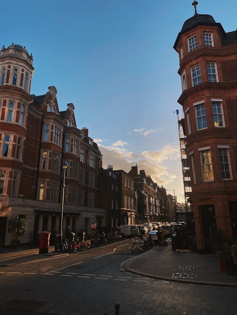 A multi-storey Victorian townhouse constructed from light brown brick with white-framed sash windows and black window grilles, situated on a narrow street in Teddington. An external metal staircase wi